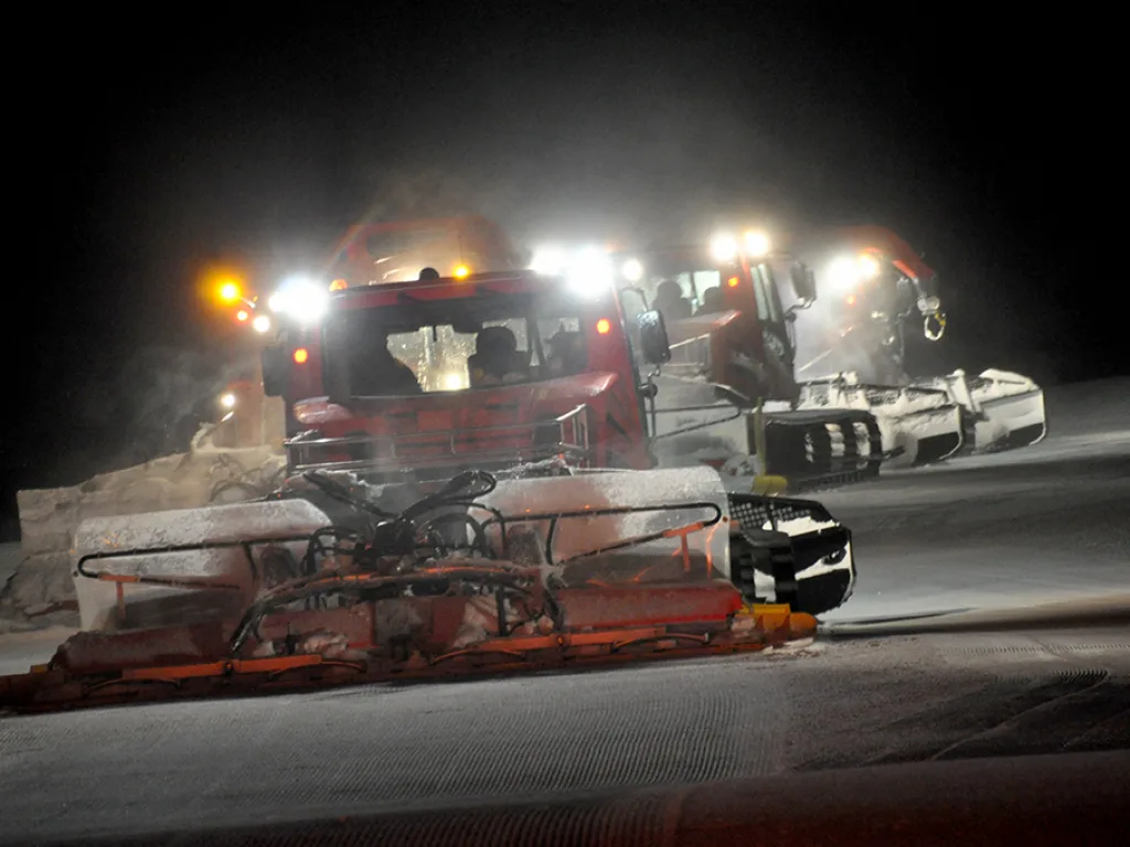 Pistenraupe im Scheinwerferlicht auf der Piste.
